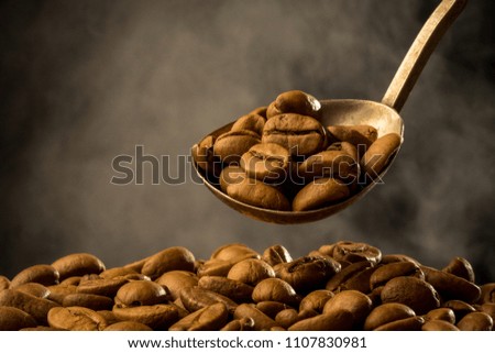 Roasted ground coffee into an old silver spoon and roasting coffee beans with smoke steam on dark background. Close-up photo. Vintage style effect picture, with copy space.