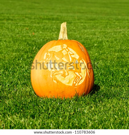 Picture of a pumpkin, with silhouette of a knight and horse cut in the surface Standing on a lawn