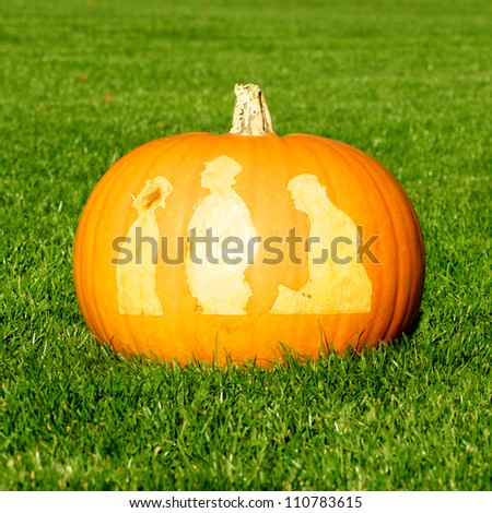 Picture of a pumpkin, with silhouettes of people cut in the surface Standing on a lawn