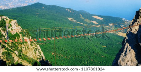 Panoramic view of hanging rope bridge between rocky mountains or cliffs at forest and sea landscape. Leisure activity at summer day background in Crimea, Ai-Petri