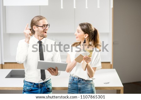 Young couple designing a new home interior standing with digital tablet and color swatches in the white kitchen interior