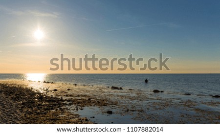 sunset at the baltic sea - a fisherman stands in the sea and catches fish