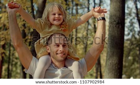 Little girl riding on dads neck at autumn park