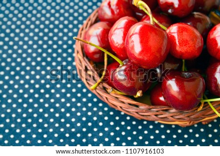 Fresh ripe organic cherries in a basket on a blue napkin with white polka dots.
Summer fruit or healthy eating concept.
Selective focus.