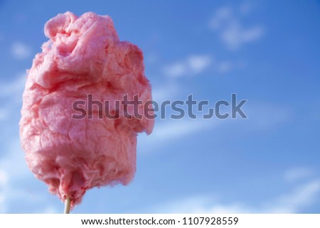 close up pink fluffy cotton candy in front of the bright blue sky with white clouds/ summer background