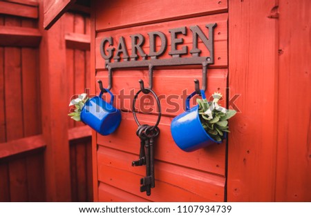 Cast iron garden lettered hooks on a bright red outdoor wooden shed with hanging white flowers in blue mugs and old vintage cast iron keys 