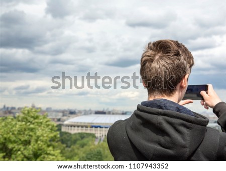 Young Man Tourist Takes Picture of the Luzhniki Stadium with Smartphone. Tourism in Russia, Panorama Moscow from Observation Deck in Sparrow Hills.
