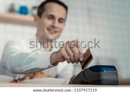 Only credit card. Handsome male person keeping smile on his face while serving his client
