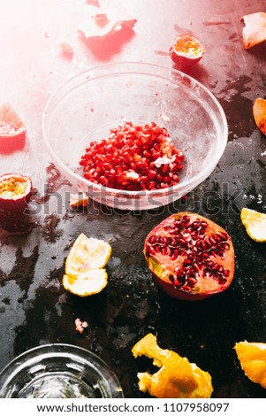 Pomegranate seeds on a glass bowl, with scattered piece of pomegranate fruit around and orange, ingredients to make a fresh summer juice,backlight flare with red colors.