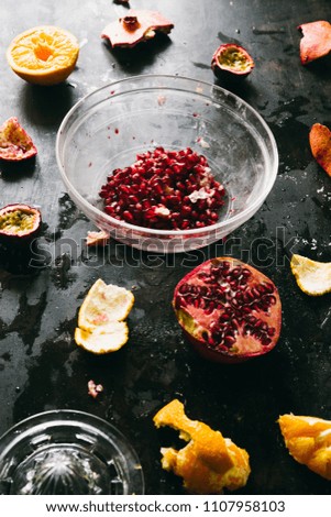 Pomegranate seeds on a glass bowl, with scattered piece of pomegranate fruit around and orange, ingredients to make a fresh summer juice