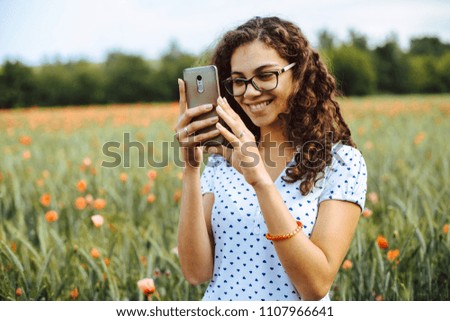 Beautiful young woman taking pictures of a poppy field with her cellphone
