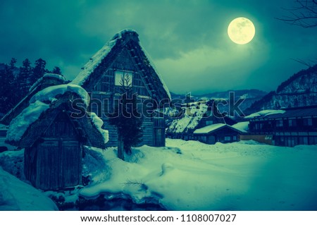 Snow covered the ground in winter season. Silhouette of town with night sky and bright full moon, serenity nature background. High contrast. Cross process. The moon taken with my own camera.