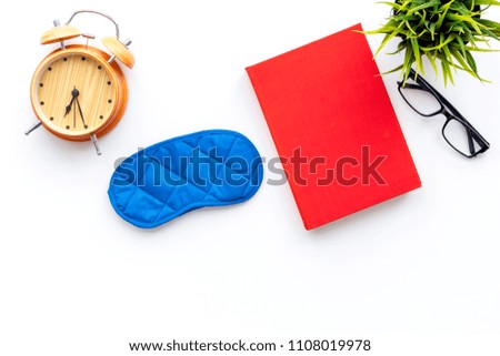 Healthy sleep concept. Sleeping mask near alarm clock and book on white background top view space for text