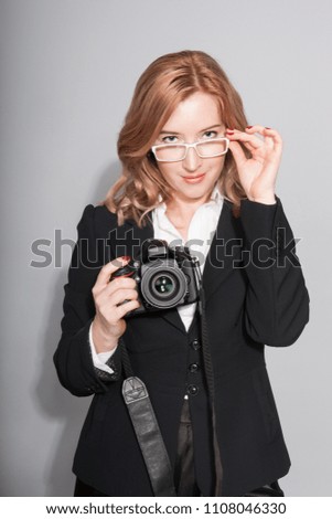 Young woman in a black business suit with a camera on a gray background in the studio