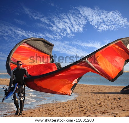 surfer on the beach with his board and  red  kite on deep blue sky background