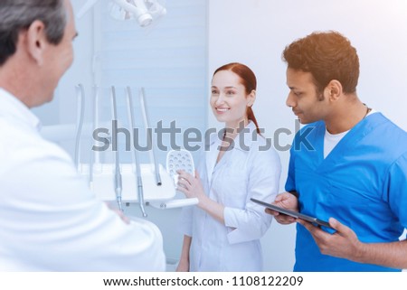 I know it. Attractive intern putting left hand on the control panel of dental equipment and keeping smile on her face while looking at mentor