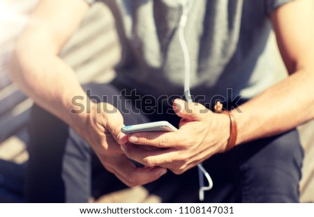 people and technology concept - close up of man with earphones and smartphone listening to music at brick wall on street