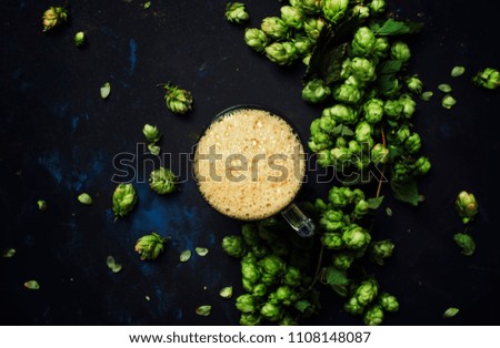 Big glass of foamy beer and hop cones on black stone background, top view