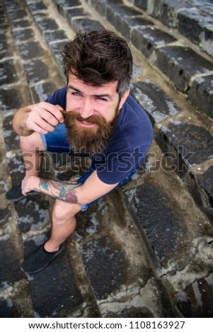 Macho with beard and mustache sitting on stone stairs background. Hipster on cheerful face relaxing outdoor. Man having rest, enjoy freshness after rain. After rain concept.