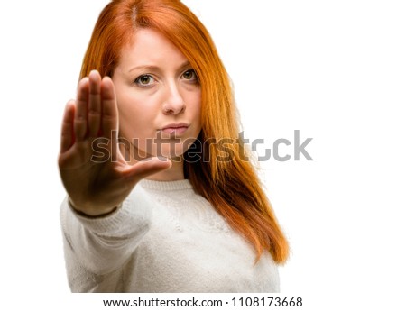 Beautiful young redhead woman annoyed with bad attitude making stop sign with hand, saying no, expressing security, defense or restriction, maybe pushing isolated over white background