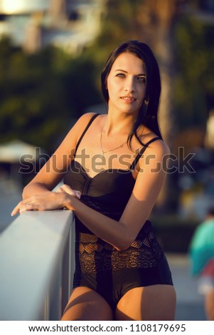 Beautiful woman wearing black bikini by the pool in summer scenery.