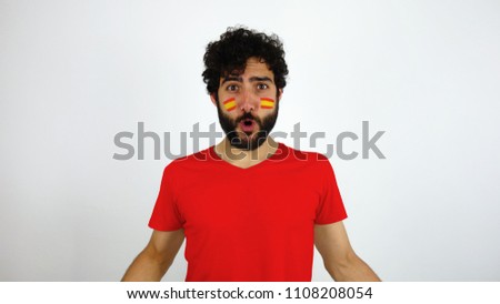 Sport fan celebrating a goal of his team. Man with the flag of Spain makeup on his face and red t-shirt.        