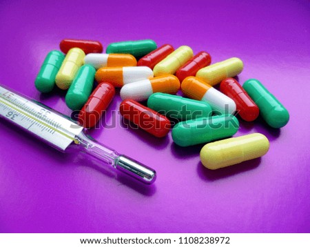 Pills. Traditional medical mercury thermometer (Celsius scale) with a color scattered pills on purple background. Close Up. Health, medicine, medical examination concept.