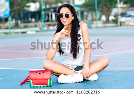 Positive summer bright portrait of young hipster girl posing at sport ground, wearing trendy casual outfit, funny watermelon bag and sunglasses.