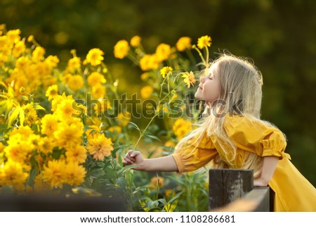 little girl in yellow dress sniffing a lot of yellow flowers Royalty-Free Stock Photo #1108286681