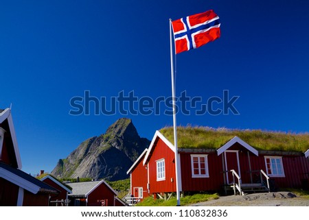Norwegian flag with typical norwegian red wooden house with sod roof on Lofoten islands Royalty-Free Stock Photo #110832836