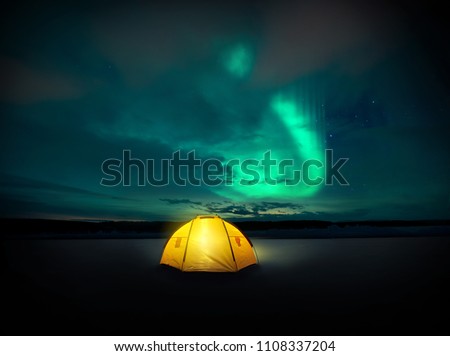 Out in the wilderness The Norther lights ( Aurora Borealis) dances across the night sky in Sweden, above the glowing lights from the camping tent. Photo Composite.