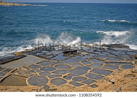 Picture of the Fresh sea water salt farm which is still being used in Malta , with the waves from the Mediterranean sea splashing against the rock.