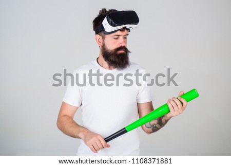 Hipster with stylish beard testing virtual reality gaming equipment. Bearded man in VR headset holding baseball bat isolated on gray background. Gamer with nerdy beard playing simulation sport game.
