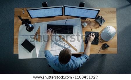 Top View of a Technical Engineer Working on His Blueprints, Drawing Plans, Using Desktop Computer. Various Useful Items Lying on his Table. Royalty-Free Stock Photo #1108431929