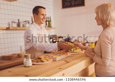 Easy payment. Charming elderly woman handing a bank card to barista, wanting to pay for her order, while exchanging smiles with him