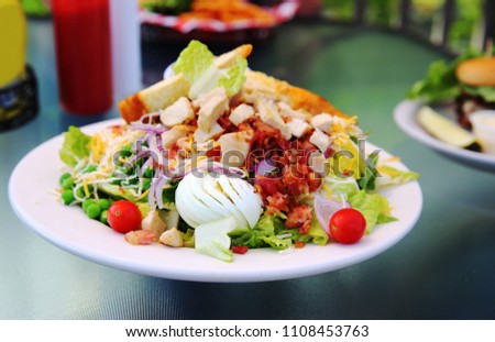 Crisp fresh lettuce with cherry tomatoes, bacon, and hardboiled egg adorn a chicken Cobb Salad