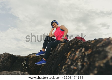 Woman sitting listening to music on the rocks in the holidays.