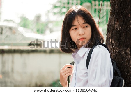 Thai cute girl student is leaning near tree and look behind