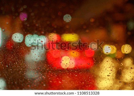 Drops Of Rain Water In Night Or Evening Street Lights On Red Glass Background. Street Bokeh Boke Lights Out Of Focus.