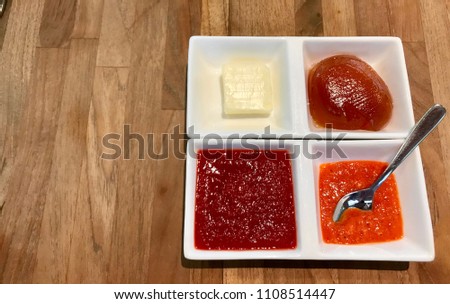 Various condiments in white square ceramic trays on wood table as seen from above. 
