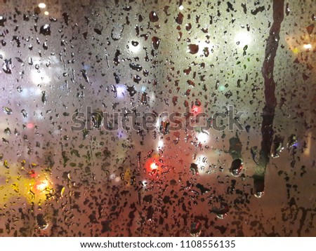 Water drops on glass of window while the rain is falling with street lights behind at night. Image with selective 