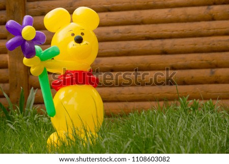 A large yellow bear from balloons with a big flower in the garde