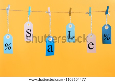 Labels hang on a rope attached with clothespins. They have the inscription SALE. Bright photo on an orange background.