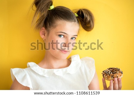Beautiful teen girl eating a donut. emotionally laughing. on a yellow yak background. summer sunny picture.