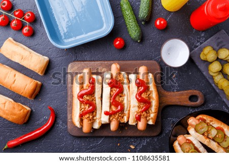 Picture on top of buns with sausages on cutting board, on table with cucumbers