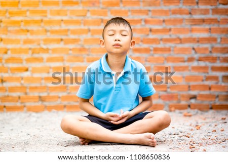 Asian cute kid sitting meditation on ground on brick wall background. Child boy thinking and brain gym. He focusing mind on a head to achieve a mentally clear and emotionally calm state
