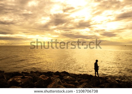 Silhouette Fisher man with fishing rod on the beach at sunset 
