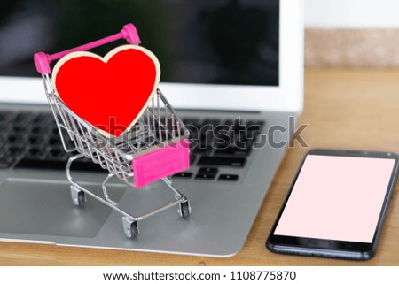 Model red heart on shopping cart on laptop with phone on wooden desk.
