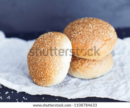 Three fresh buns on the butter-paper on the black background