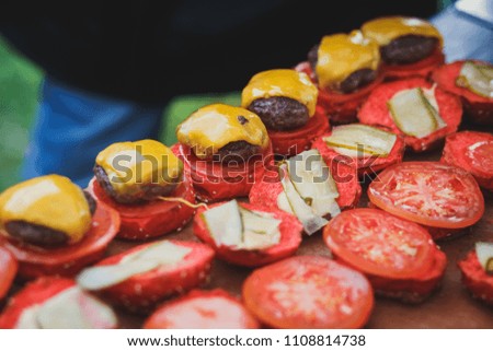 Process of cooking different multi colored burgers on open-air festival, view of chef hands in black gloves with variety of fillings and ingredients on wooden desk and stove